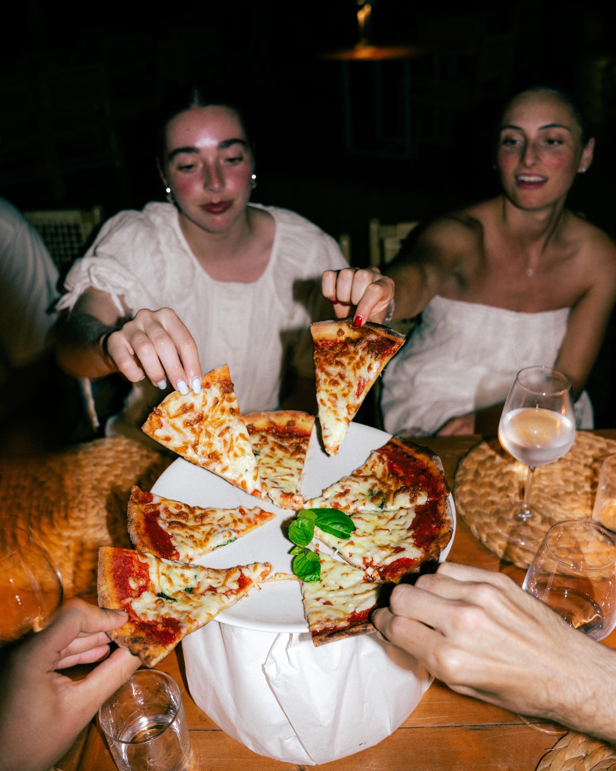 Friends reaching for slices of a Loopini margherita at dinner